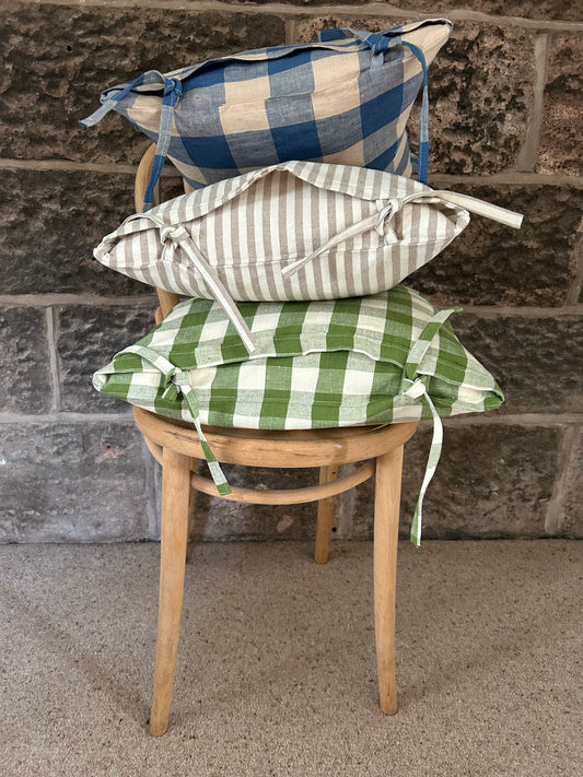 Wooden chair with three different patterned tie-top cushions against a stone wall. 